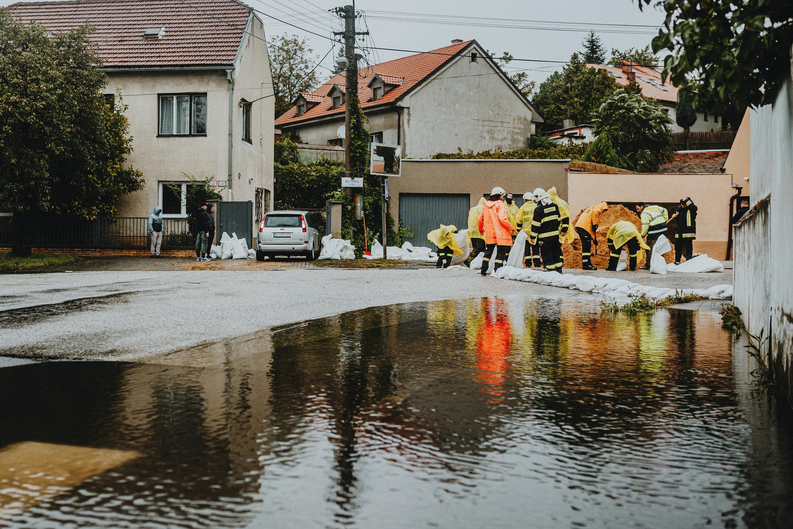 Emergency responders in reflective gear addressing floodwaters on a residential street.